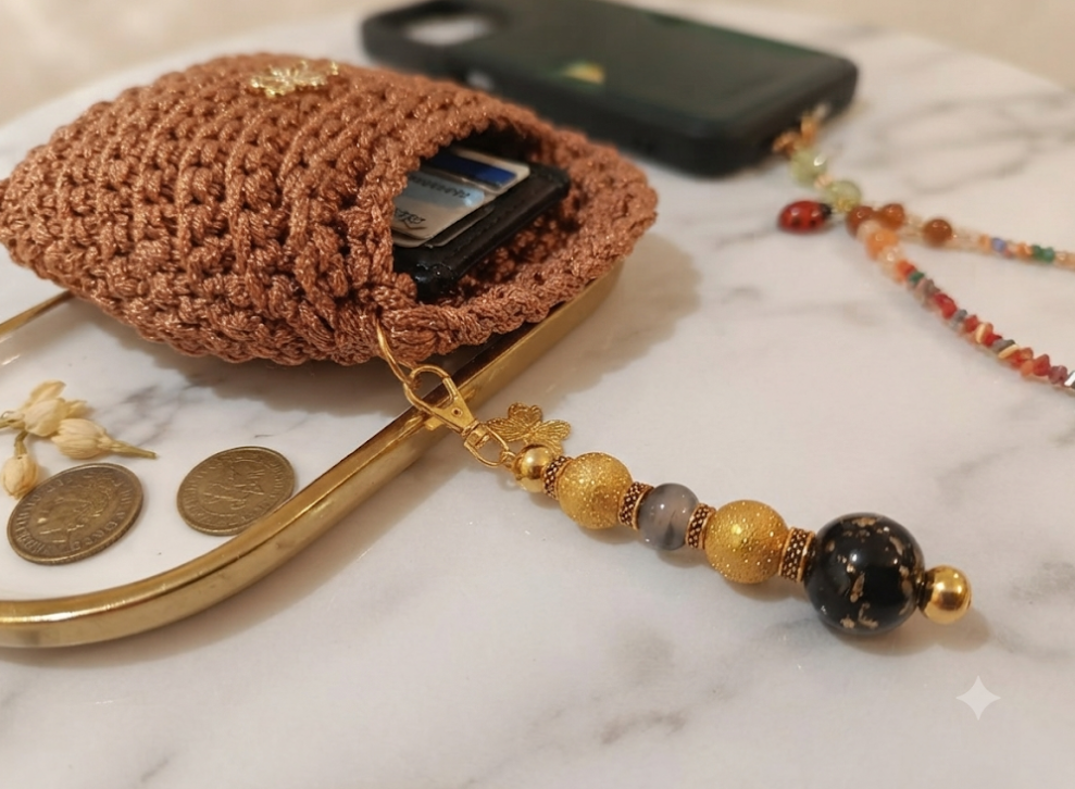 Mini Pochette Rame aperta con carte e monete visibili, chiusura a cornice dorata e pendente con pietre oro e nere su marmo bianco