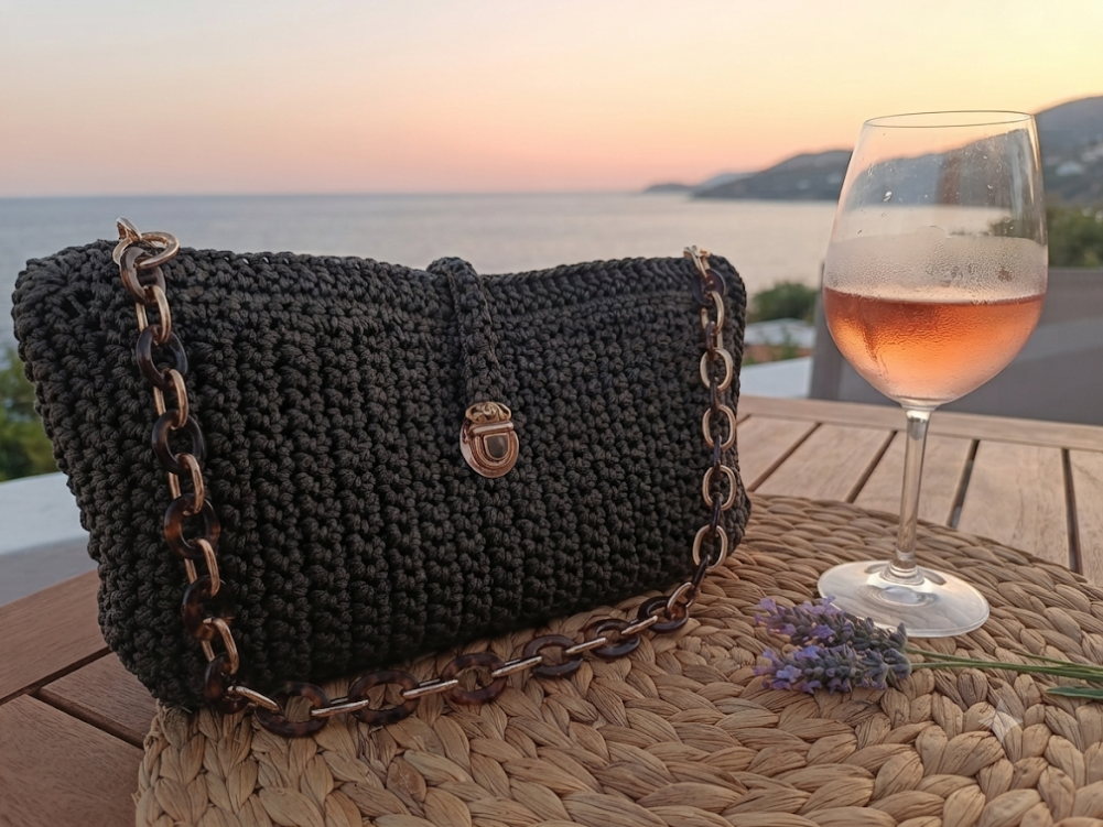 Pochette Talpa su tavolo in vimini al tramonto con calice di vino rosato e vista mare