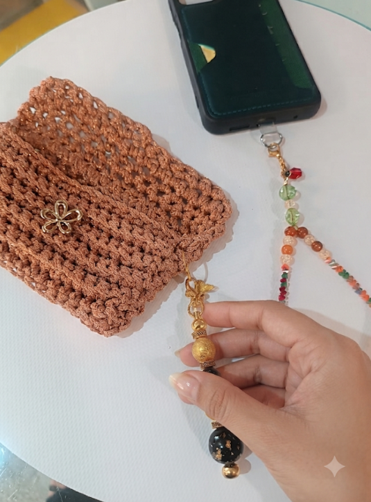 Mini Pochette Rame aperta con pendente farfalla e bracciale cristalli su tavolo bianco accanto a un telefono