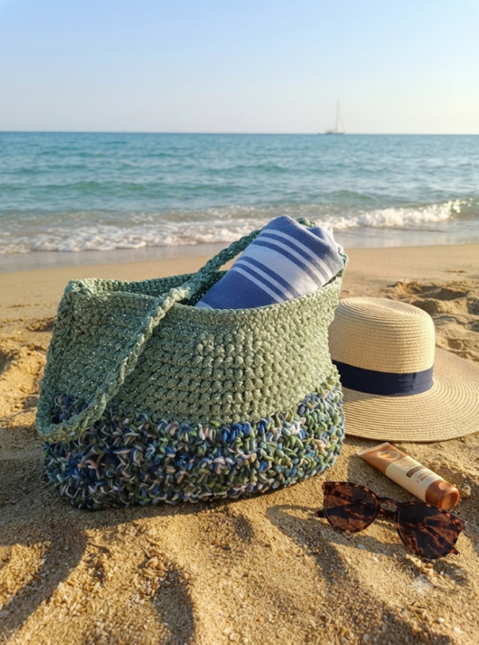 Borsa Verde Mare in rafia e tulle iridescente sulla sabbia con telo a righe e cappello di paglia