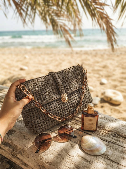 Pochette Talpa in cordino all'uncinetto con tracolla dorata sulla sabbia in riva al mare