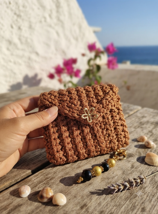 Mini Pochette Rame in tulle iridescente con bottone fiore dorato e bracciale cristalli multicolor su tavolo in legno con bouganville sullo sfondo